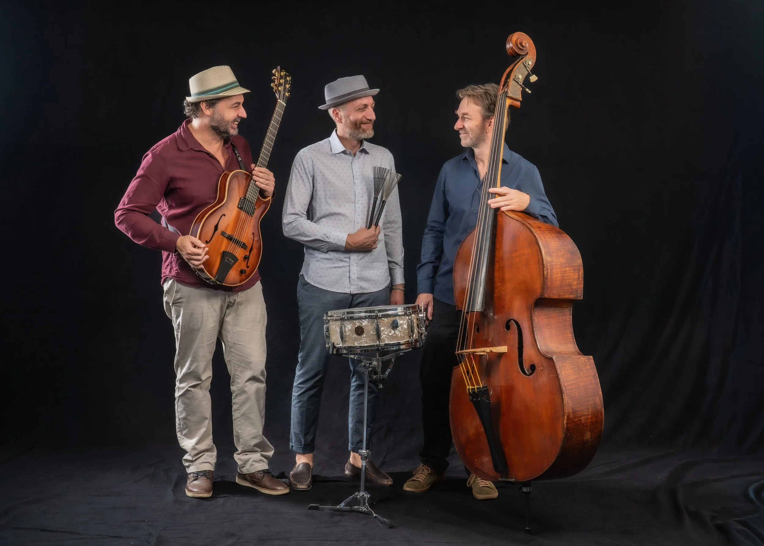 Drei Männer mit Musikinstrumenten, die sich auf einer schwarzen Kulisse unterhalten.