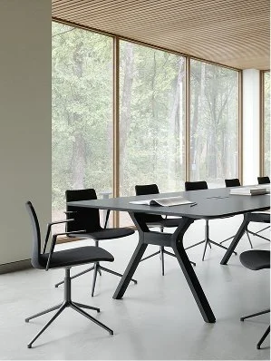 Modern conference room with a large table, office chairs, and floor-to-ceiling windows showing trees outside.