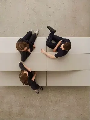 Two women sitting on a white bench, viewed from above, talking and looking at each other.