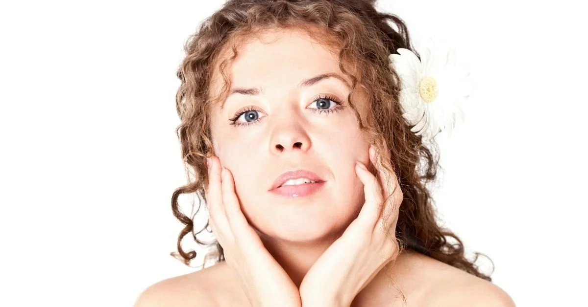 woman holding face and looking at the camera with clear skin and brown curly hair