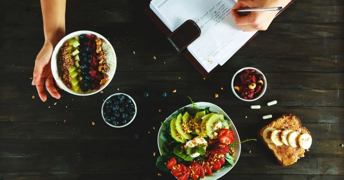 flatlay of delicious healthy and colourful food alongside a person's hand writing into a diary