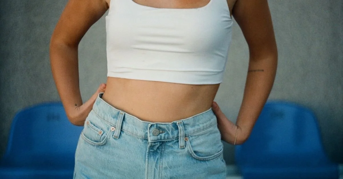 woman wearing white vest and jeans showing her midriff