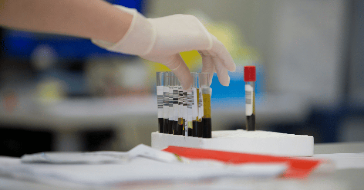 gloved hand reaching to pick up a blood vial
