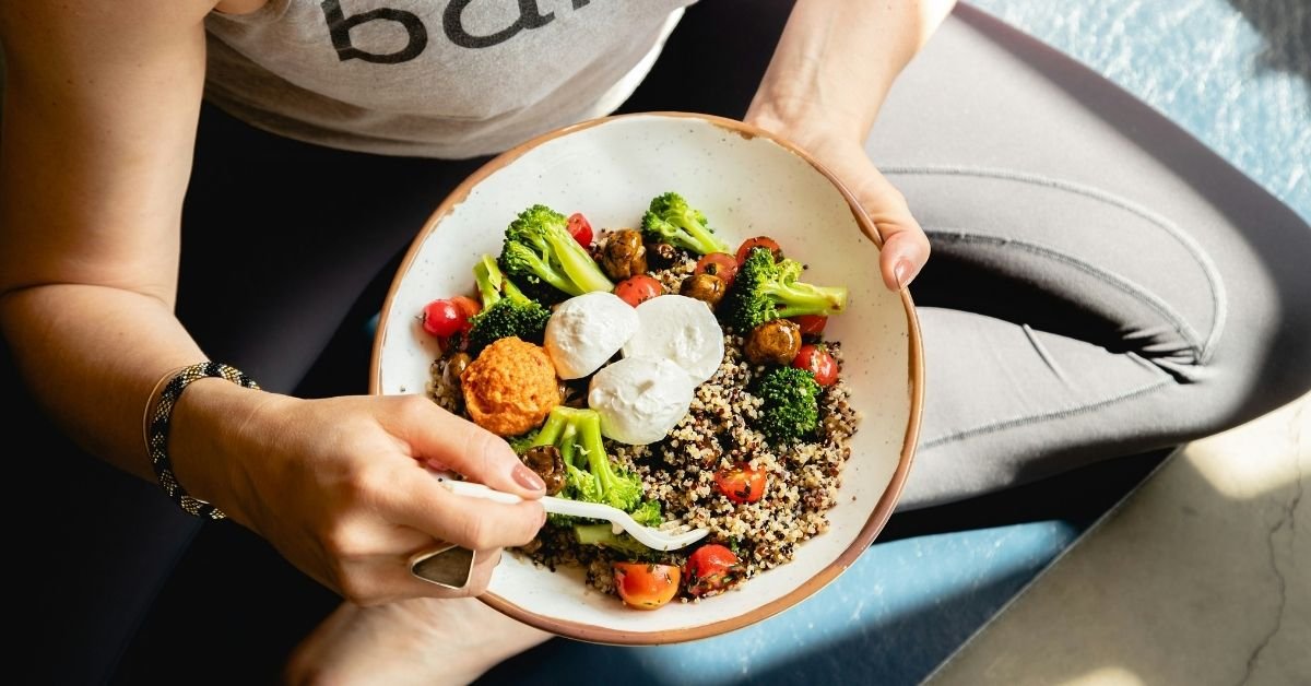 woman sitting crossed legged on the floor eating bowl of fibrous food.