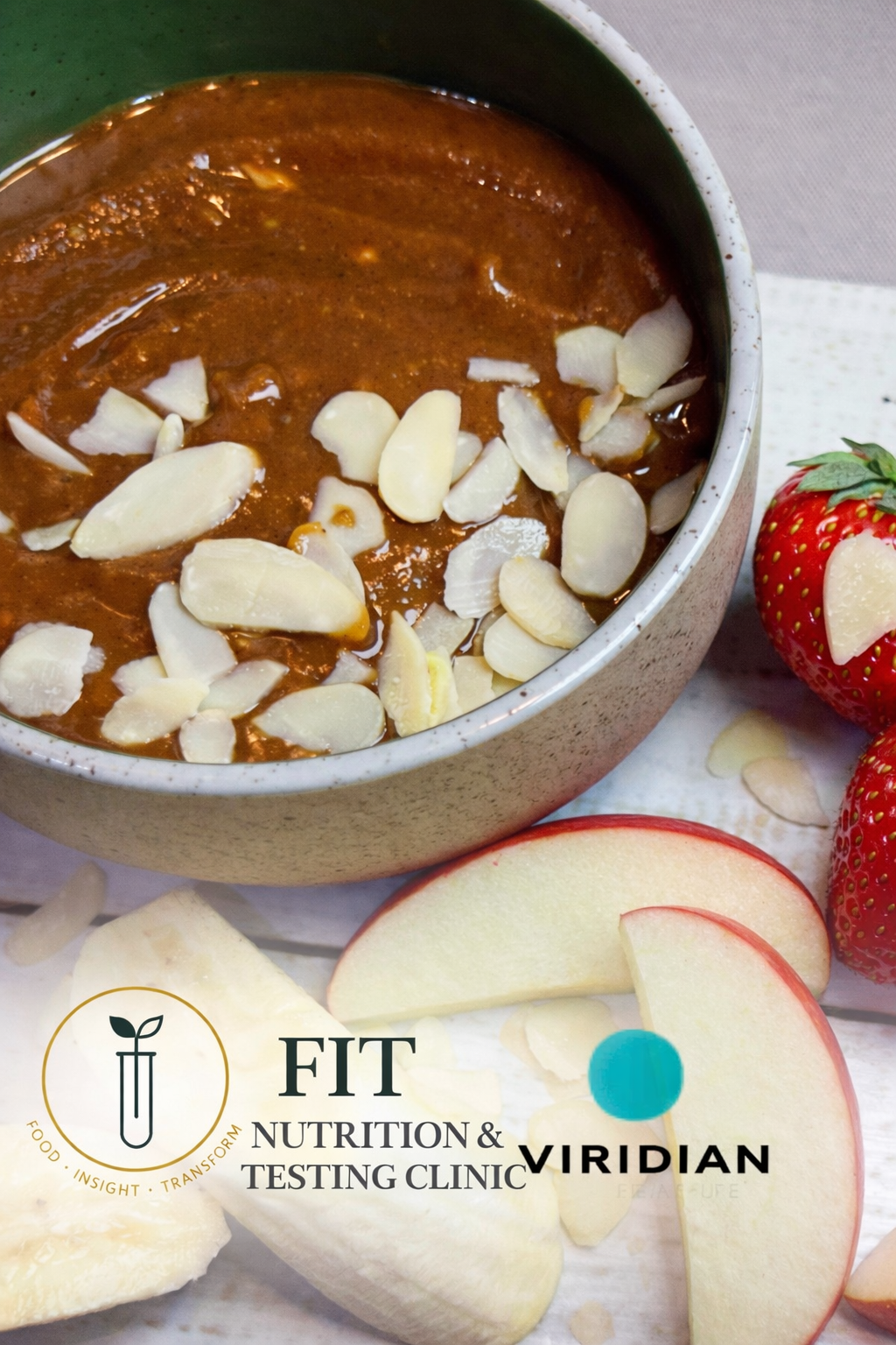 FIT miso caramel almond dip in a speckled ceramic bowl topped with toasted flaked almonds, served with fresh apple wedges, banana and strawberries