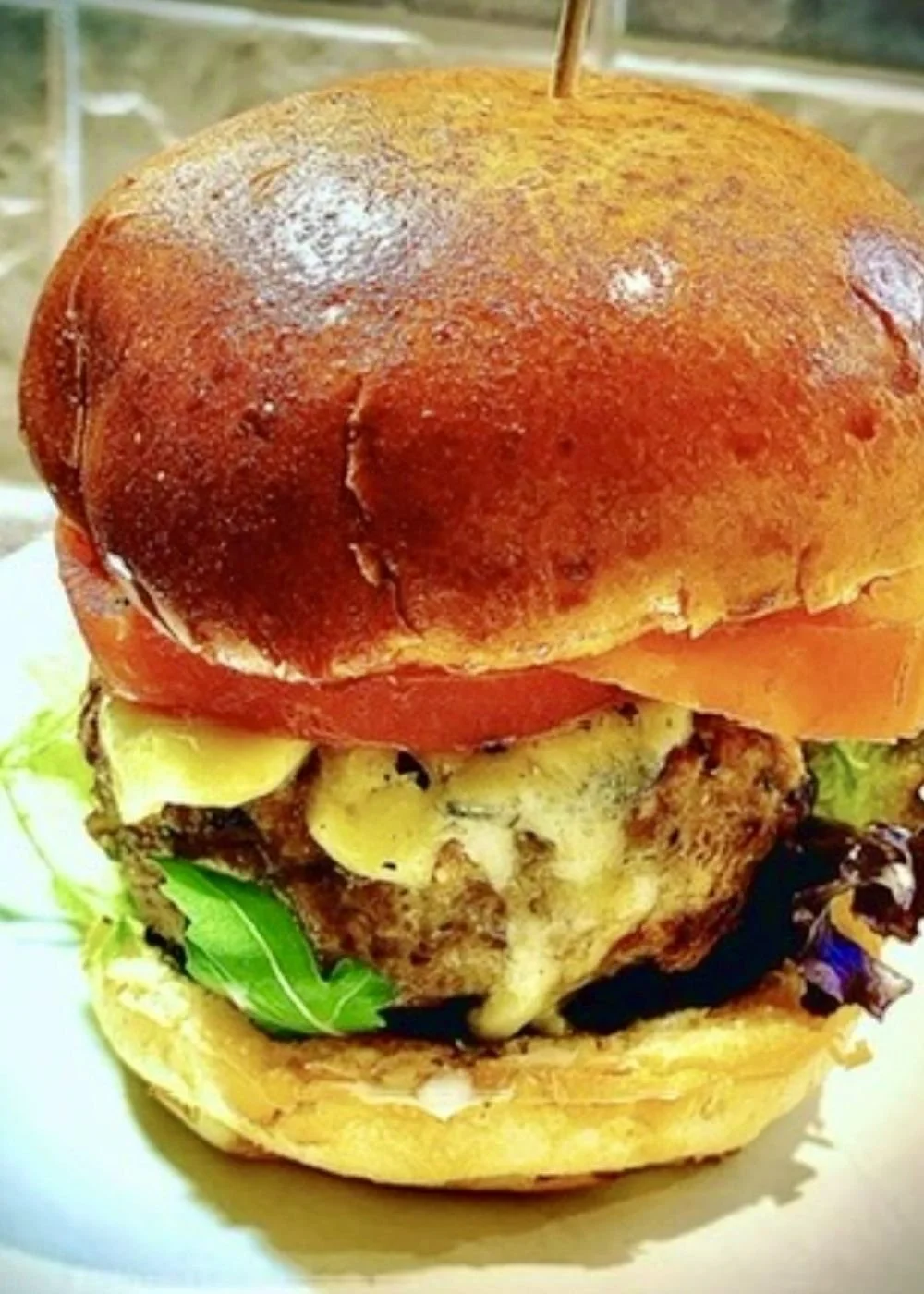 FIT-style gluten-free chicken smash burger with melted sheep's cheese, mixed leaves and tomato on a brioche bun