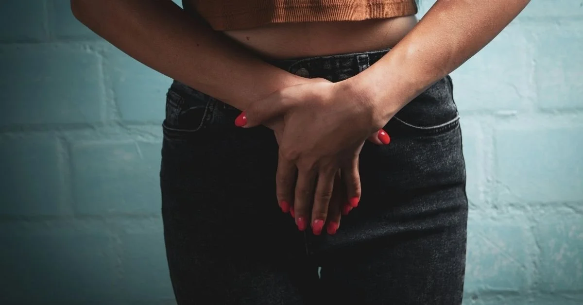 close up of woman's crotch, wearing black jeans, and her crossed hands over her crotch with painted red nails