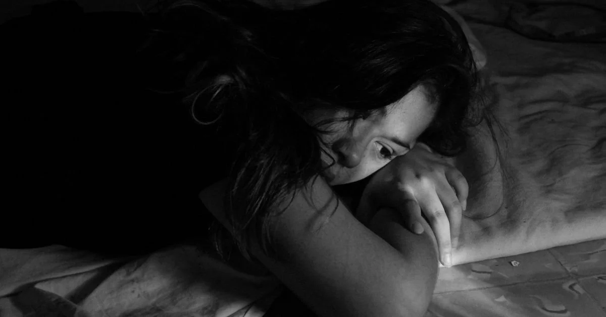 black and white image of woman lying on bed, with sad look on her face