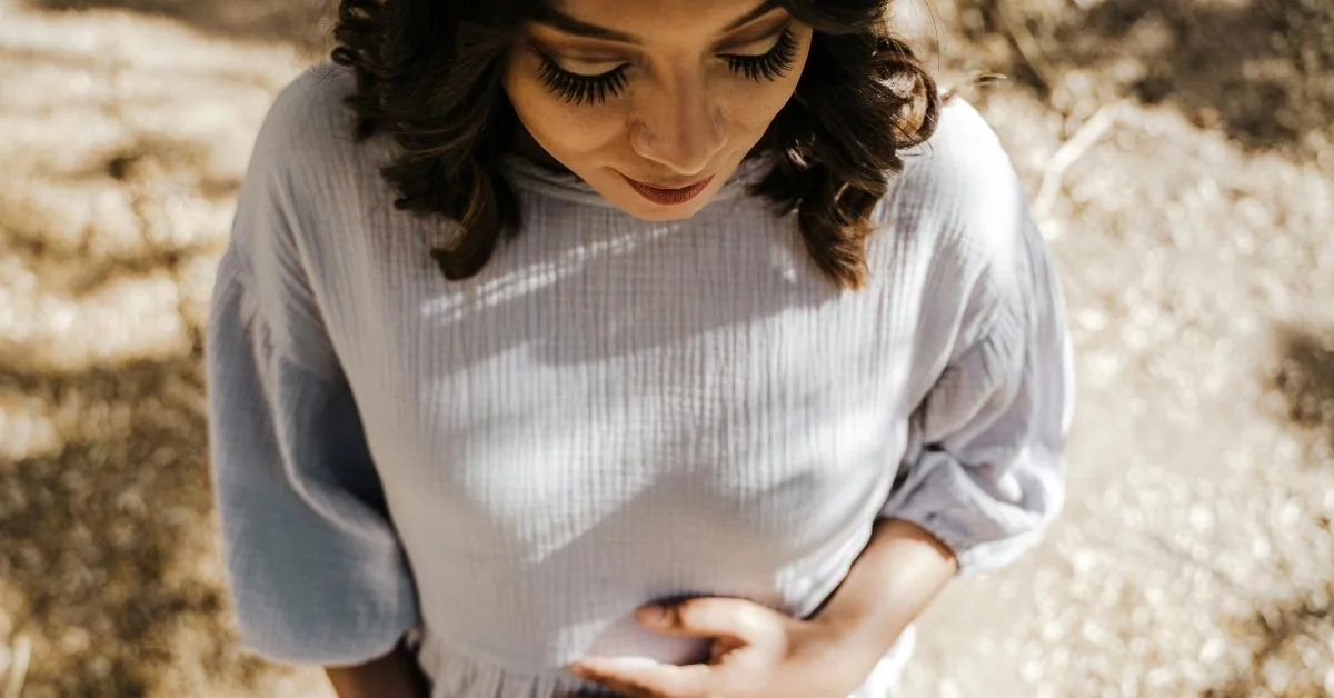 woman with dark hair looking downwards and clutching her stomach to indicate an upset