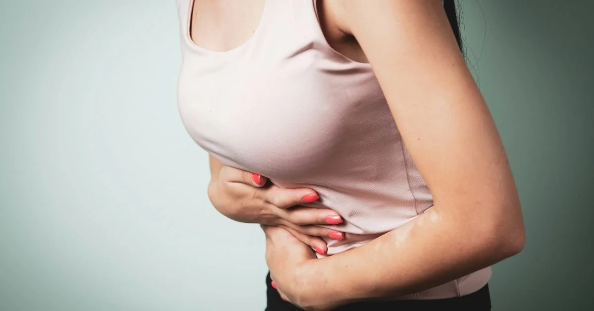 torso shot of woman in pink vest clutching her stomach