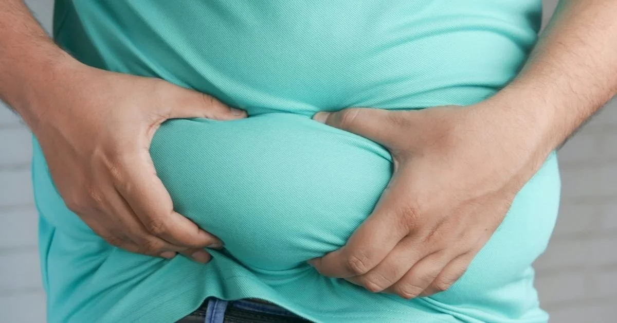 close up of man pinching belly fat. wearing turquiose t shirt