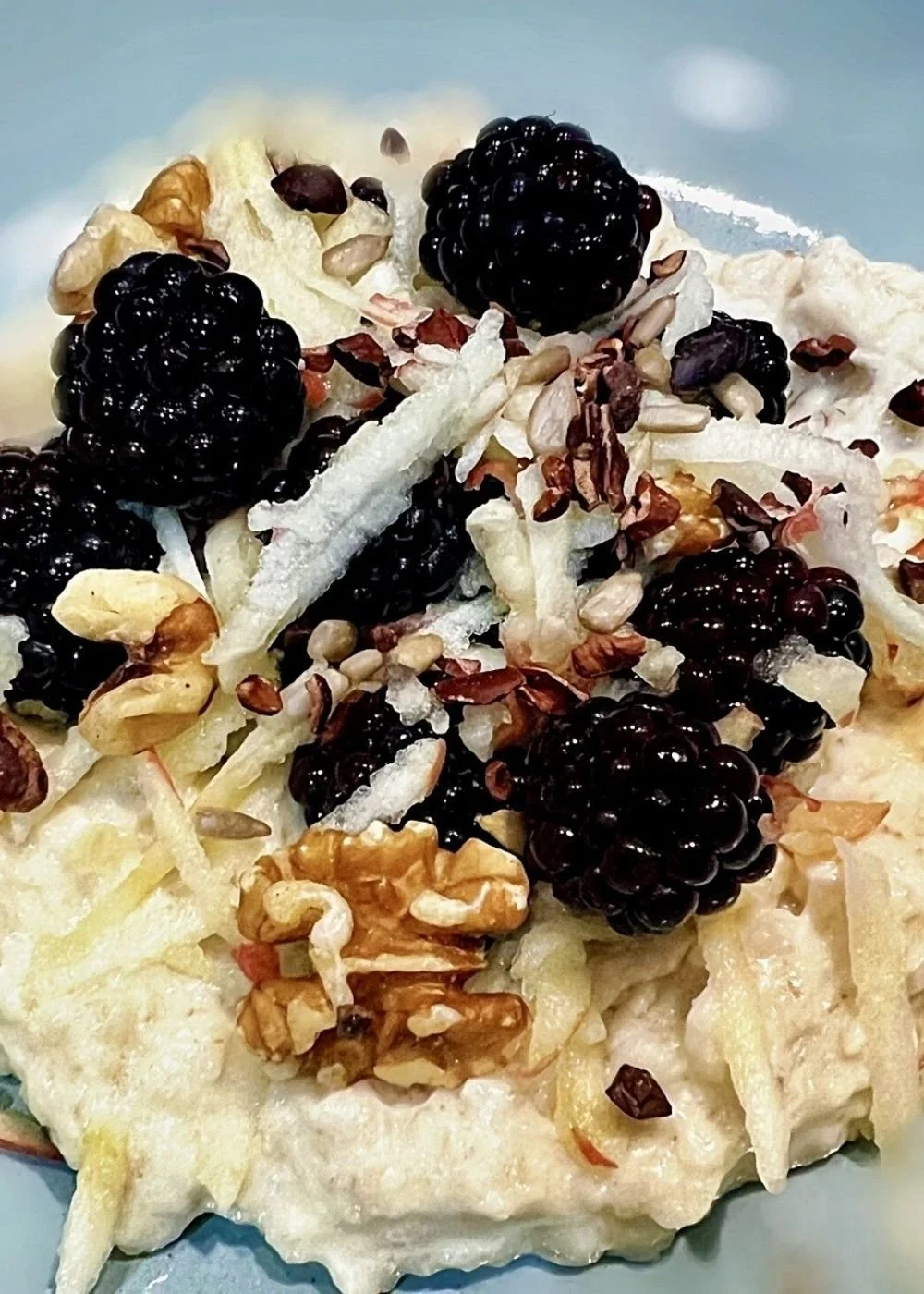 FIT spiced apple and blackberry overnight oats topped with walnuts, mixed seeds and cacao nibs in a bowl