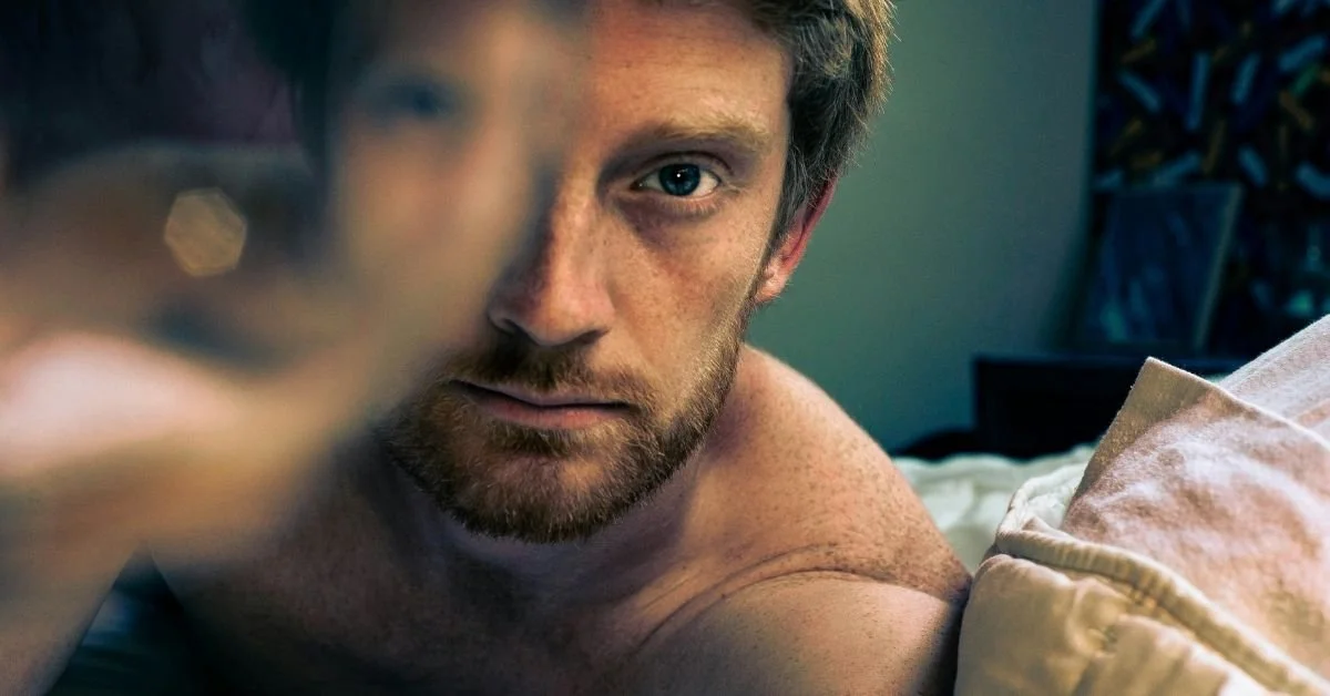 man looking into the camera, his right eye is obscured by glass so it looks blurry