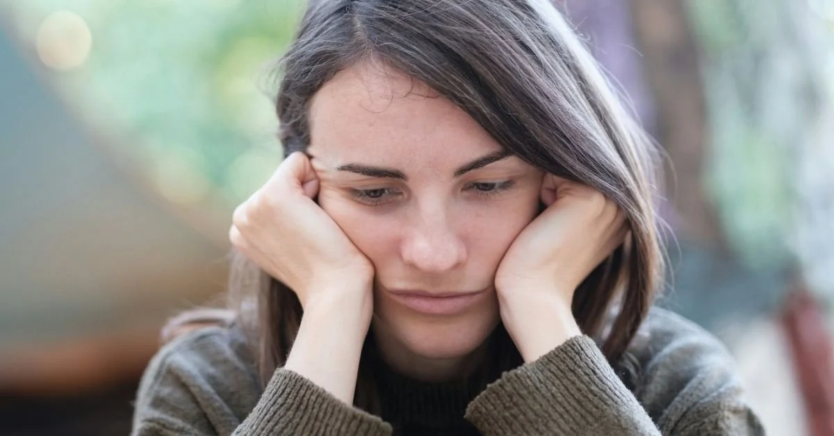 woman resting head on hands, looking downwards with a very glum expression