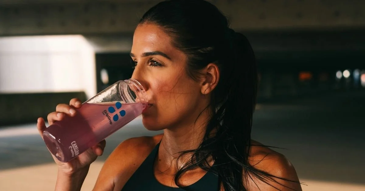 close up of woman in sports vest, drinking a sports drink