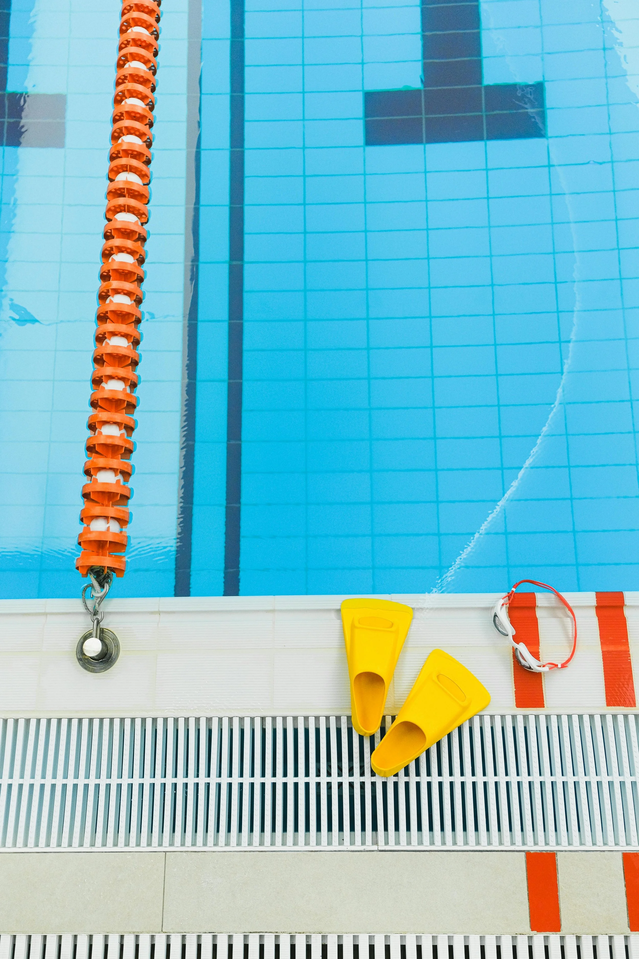 View of a swimming pool edge with yellow swim fins, red and white lifeguard float, and pool lane lines.