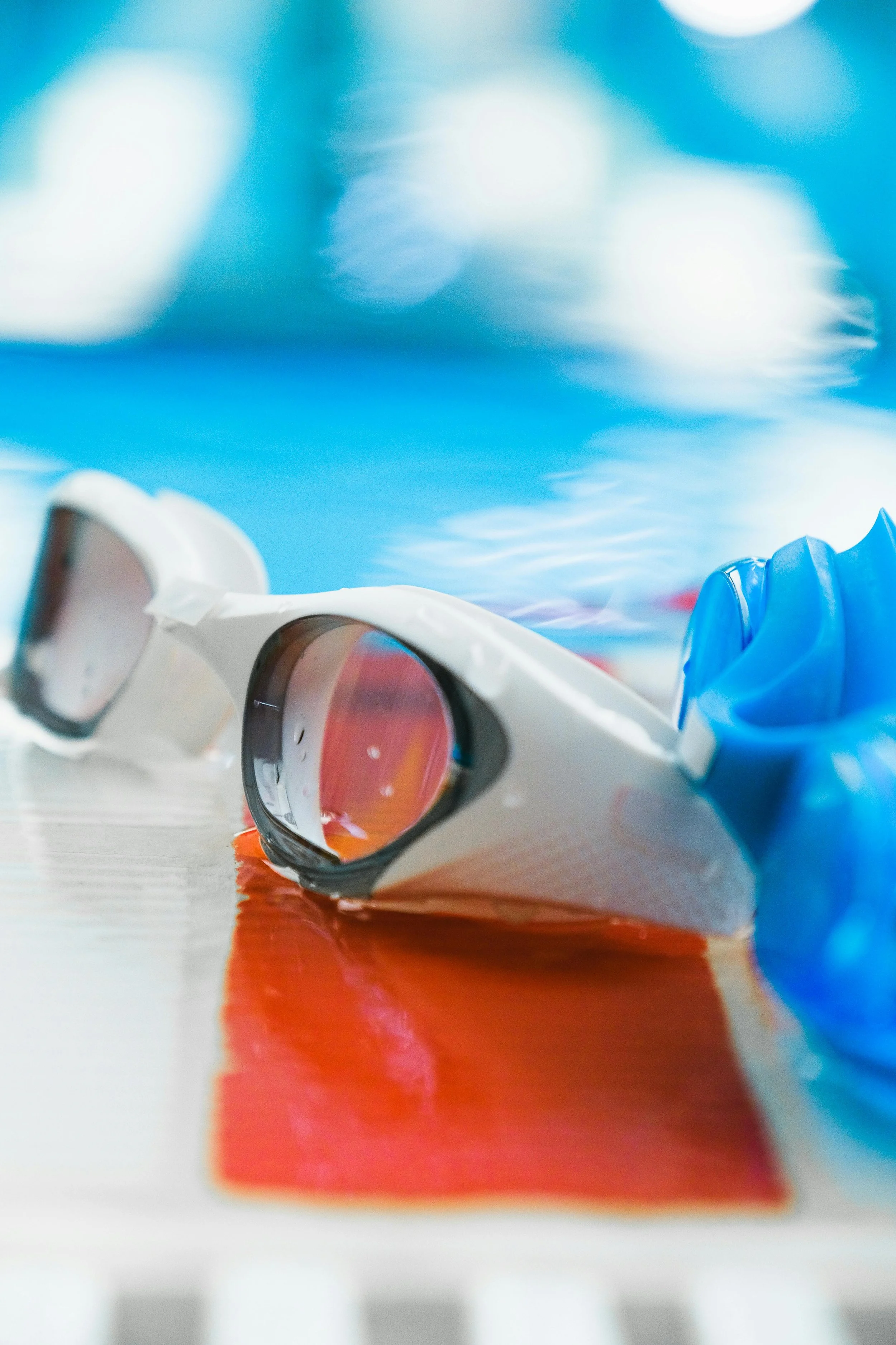 A pair of swimming goggles with a blue and white strap lying on a swimming pool deck.