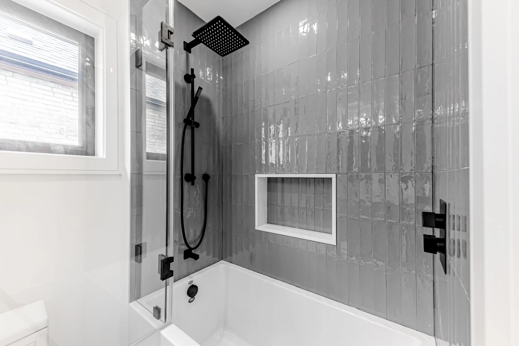 Modern walk-in shower with gray tiled walls, black fixtures, a rainfall shower head, a handheld shower, a built-in niche, and a window. bathroom renovation
