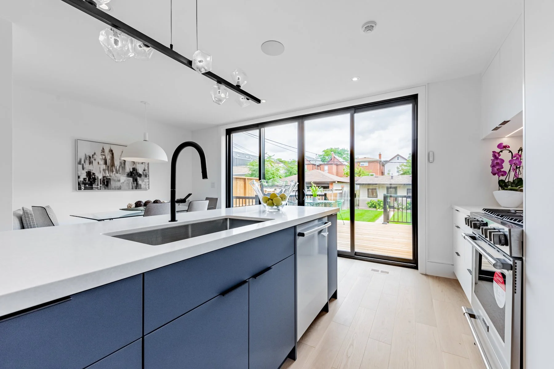 Modern kitchen renovation with a blue island, white countertops, black faucet, and a view of a backyard through large sliding glass doors. Includes a range stovetop