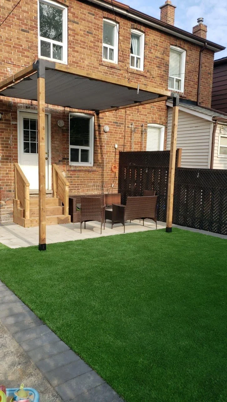 Backyard renovation with a patio with artificial grass, outdoor seating, and a new wooden pergola attached to the brick house.