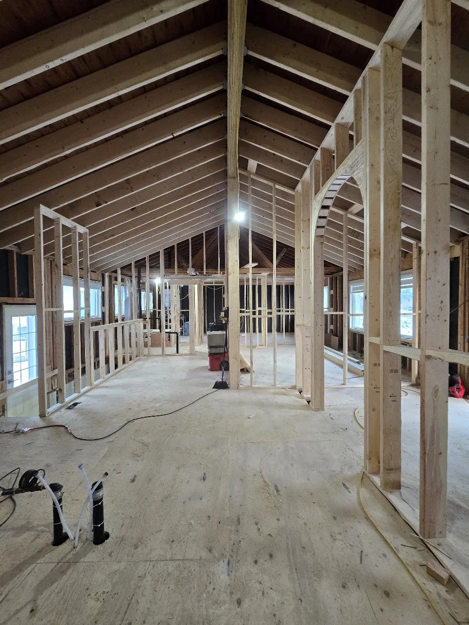 Interior view of a house under construction with exposed wooden framing and a sloped roof, with some windows installed along the walls.