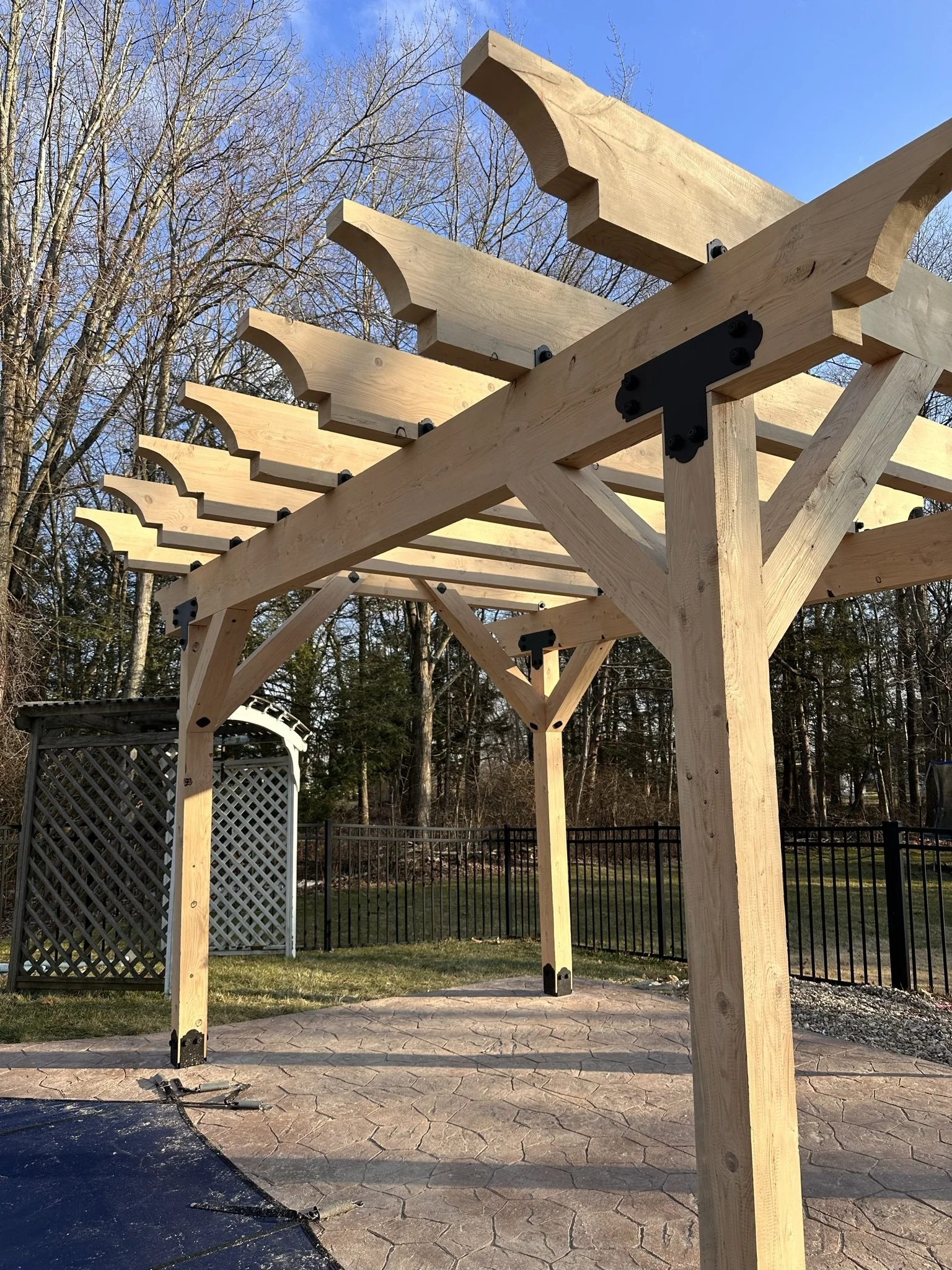 Wooden pergola under construction on a stamped concrete patio in a backyard.