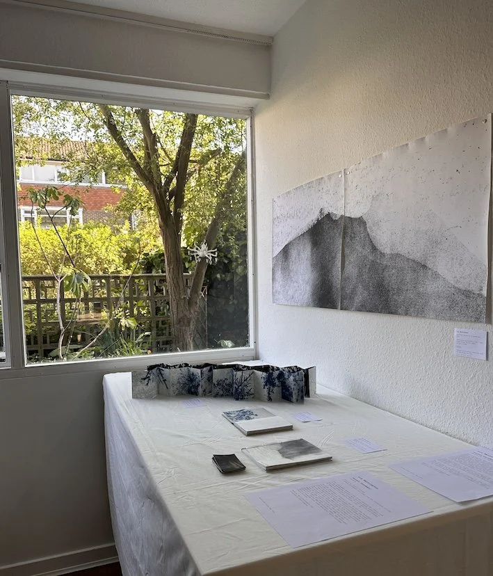 table top with artists concertina books and black and white photo on the wall