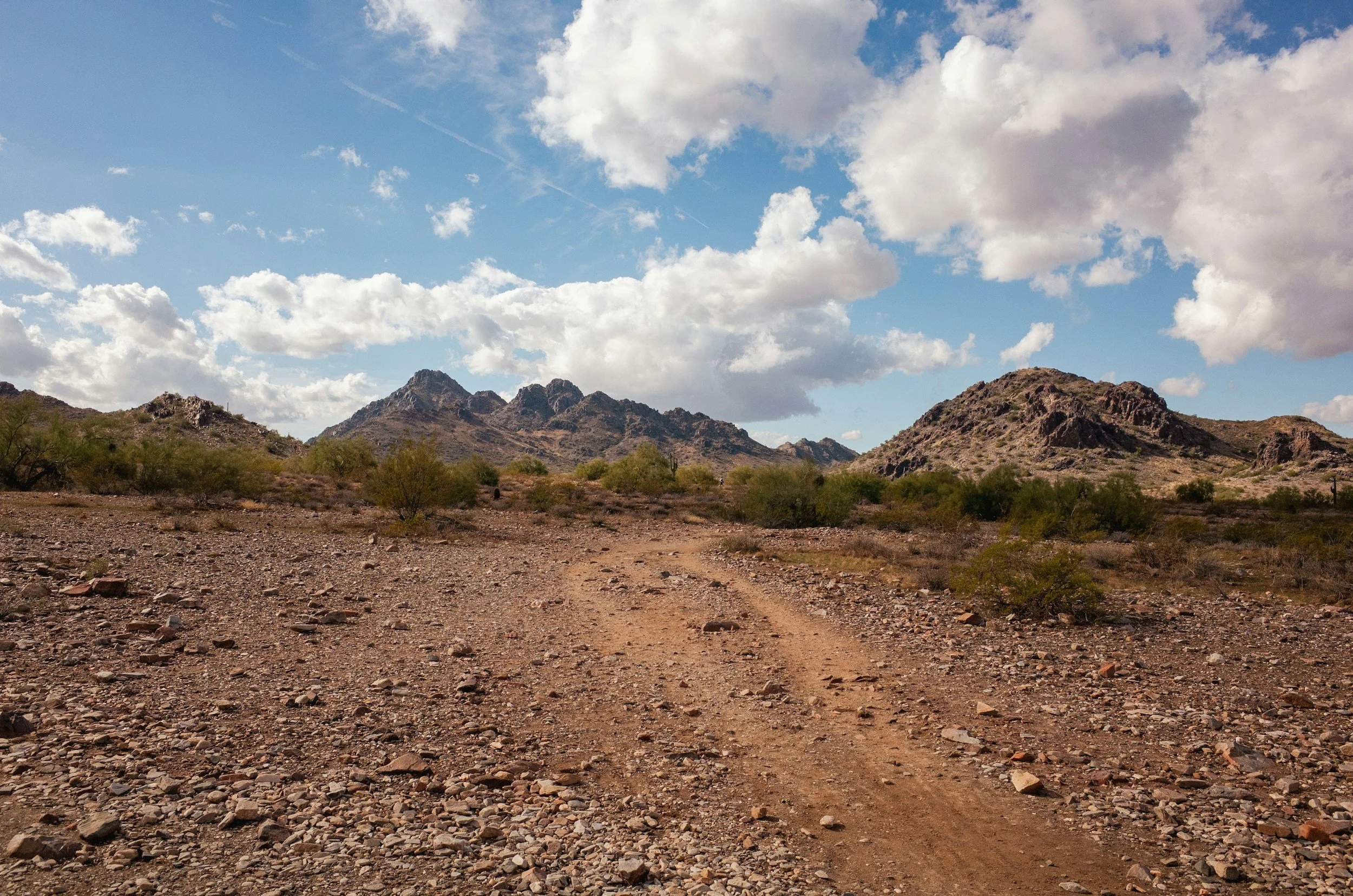 Desert trail leading toward mountains beneath a cloudy sky.