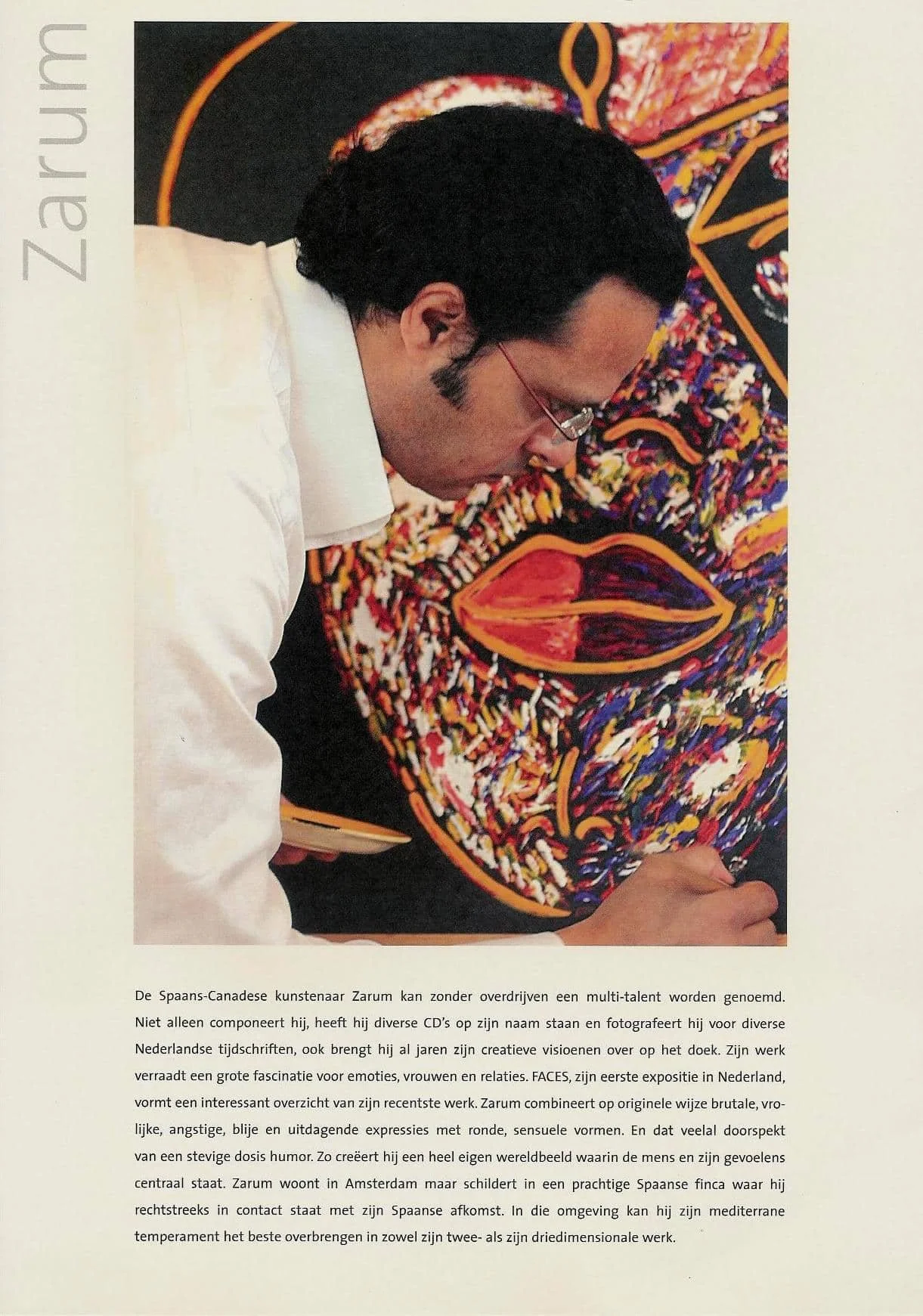 Photograph of the artists Zarum, leaning over and working on a colorful abstract artwork that features a large, stylized face with prominent lips. The artwork is vibrant with reds, oranges, yellows, and blues.