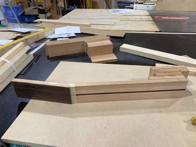 Woodworking workshop with cut and assembled pieces of wood, clamps, and tools on a workbench.