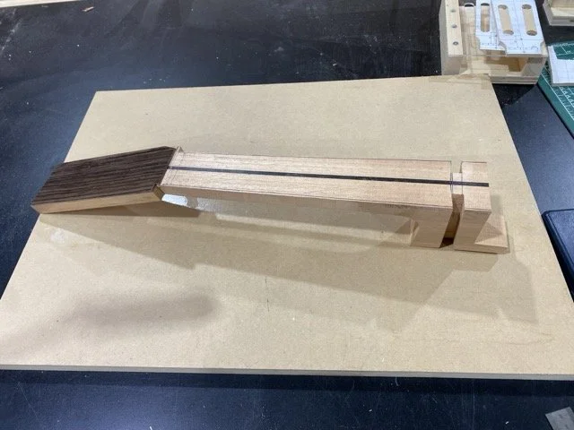 The neck blank showing the rosewood head plate glued as well as the slots for the sides which have been carved out with a chisel. Also seen is the ebony strip inserted into the neck to add stability.