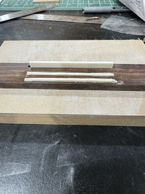 After the slots are cut into the bridge blank the bone saddle and other bone components are fitted. You can see the bone here is at the rough shape stage.