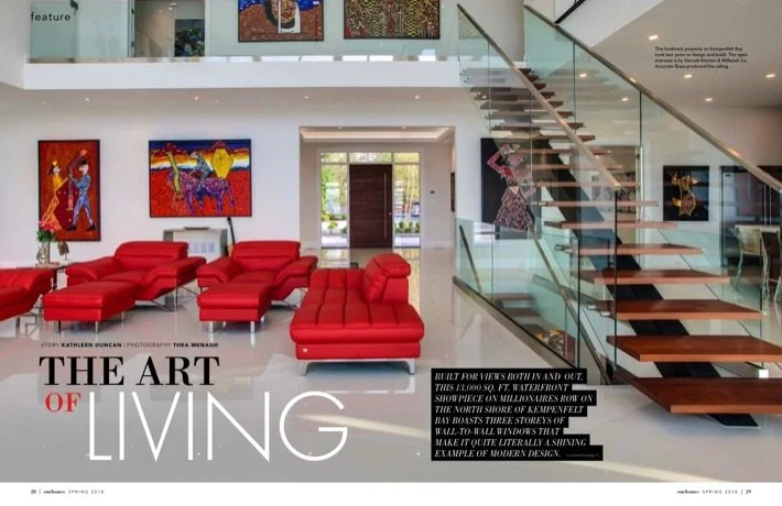 Zarum landmark home featured in a magazine. Modern interior living room with white walls, red sectional sofas, colorful artwork on the walls, and a glass staircase.