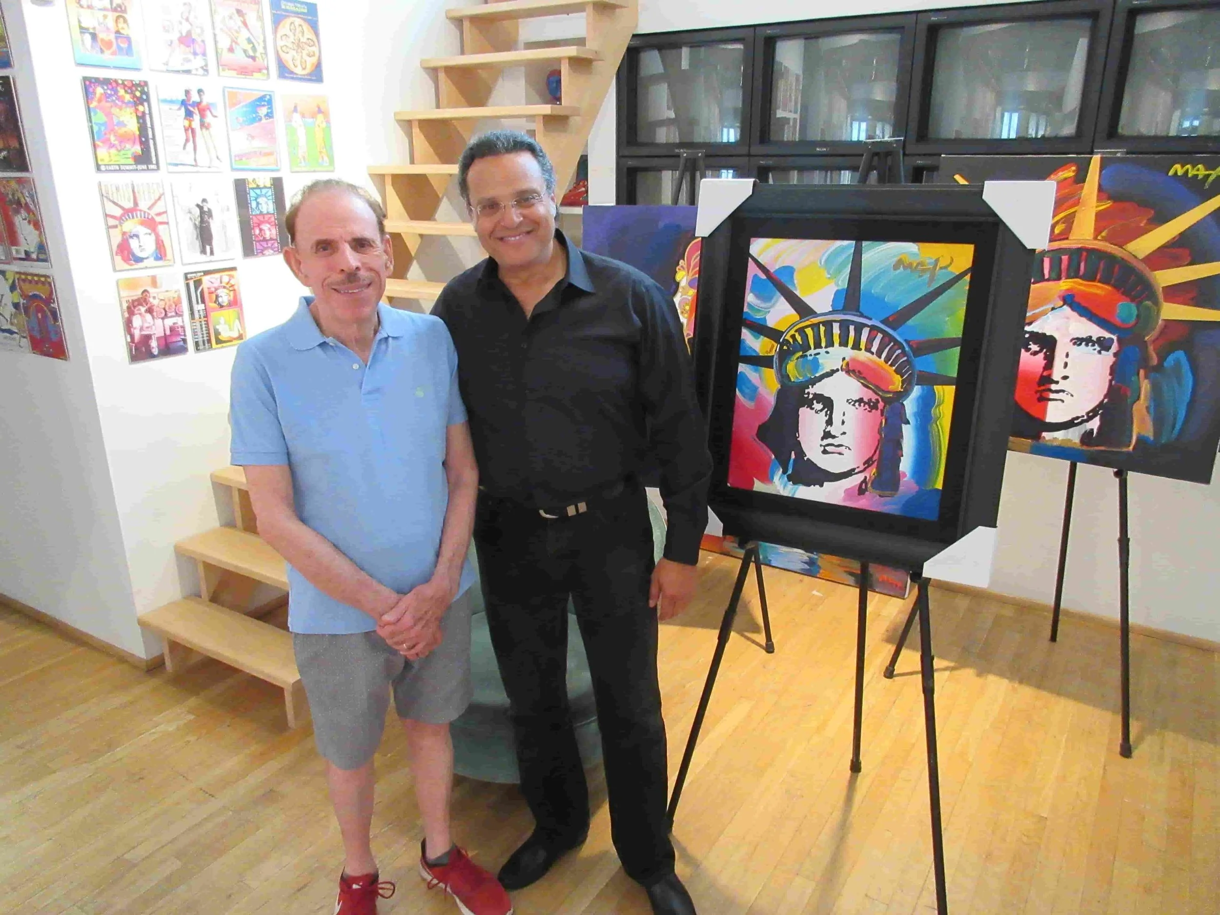 The artist ZARUM with the artist Peter Max in his New York Studio. Behind them are colorful abstract portraits of the Statue of Liberty on display, with one on an easel.
