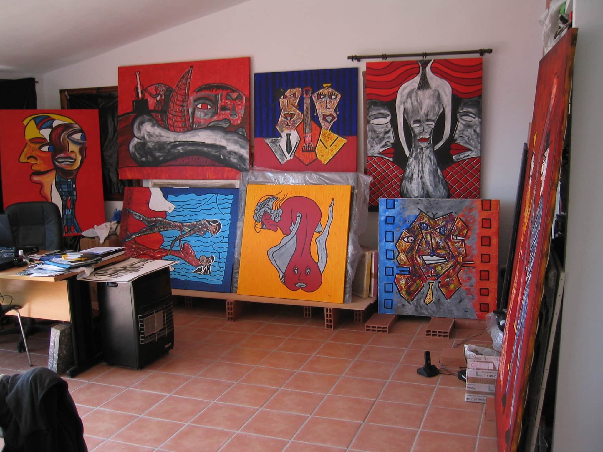 Inside Zarum's art studio in Spain with colorful abstract paintings leaning against the wall and standing on the floor.  The paintings feature bold shapes and vibrant colors, including red, blue, yellow, and black.