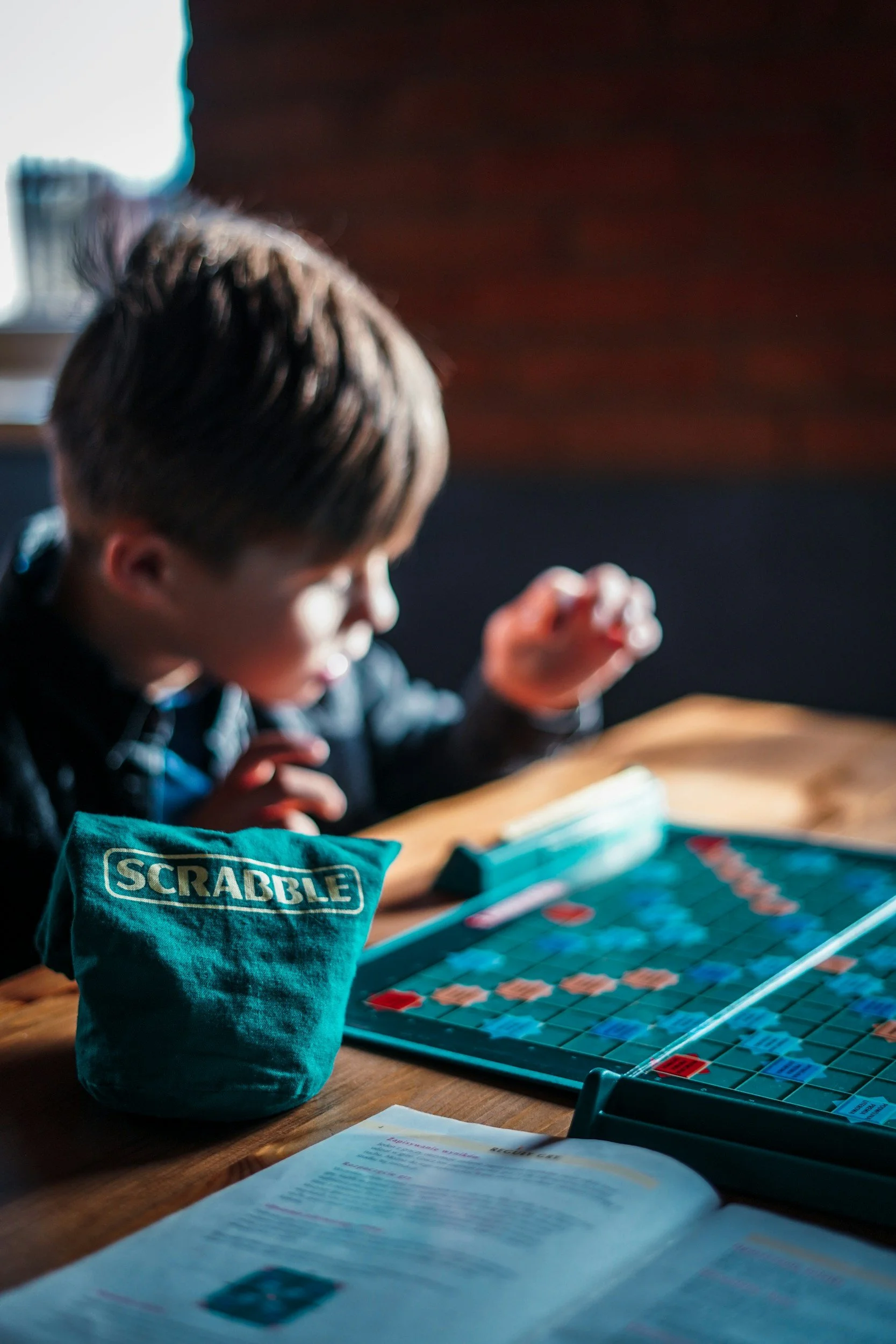 Un enfant joue à des jeux de société comme le Scrabble. L'enfant est concentré, avec une lumière naturelle éclairant le jeu et la table en bois.