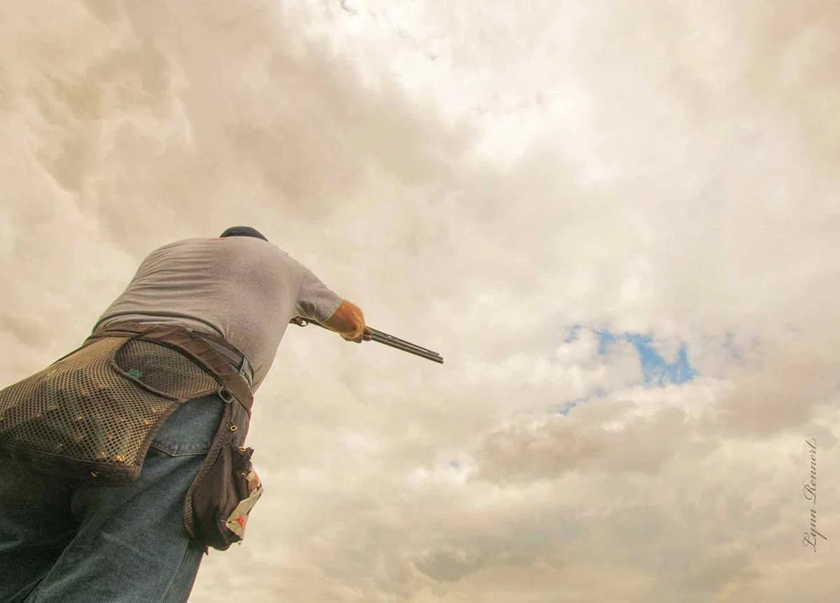 A man shooting a shotgun into a cloudy sky.