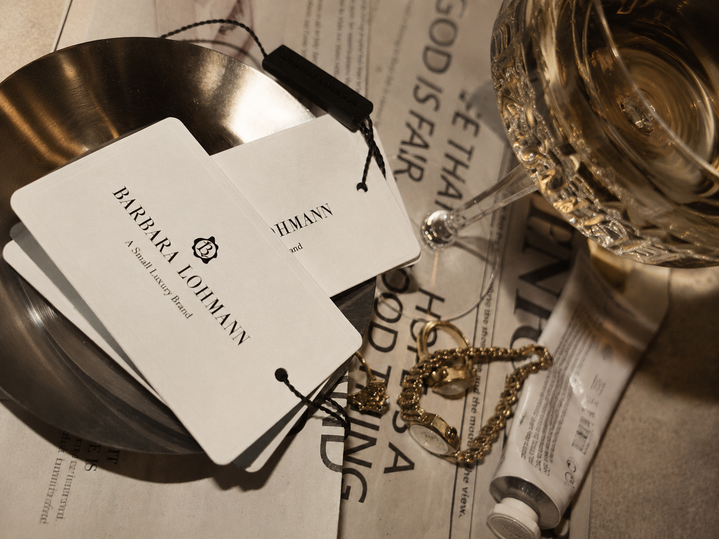 Atelier Onyx - Ein Glas Champagner, eine Goldkette, eine Uhr, zwei Karten mit dem Schriftzug «Barbara Lohmann», ein Messbecher aus Metall, eine Tube Cremes sowie eine Zeitung