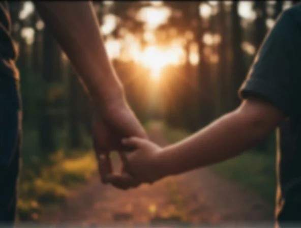 A person and a child holding hands while walking outdoors at sunset.