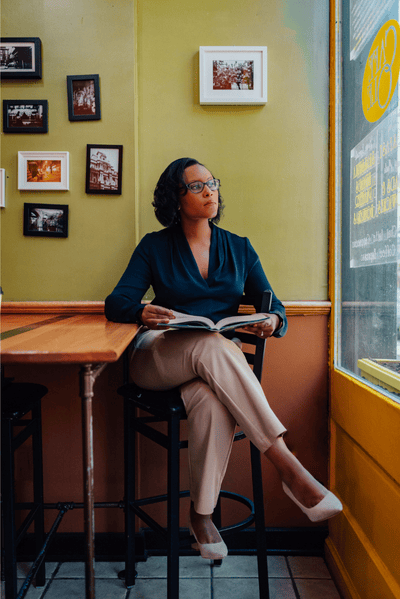 Author Ashton Lattimore with dark hair and glasses sitting by a window in a cafe, reading a book with a relaxed expression.