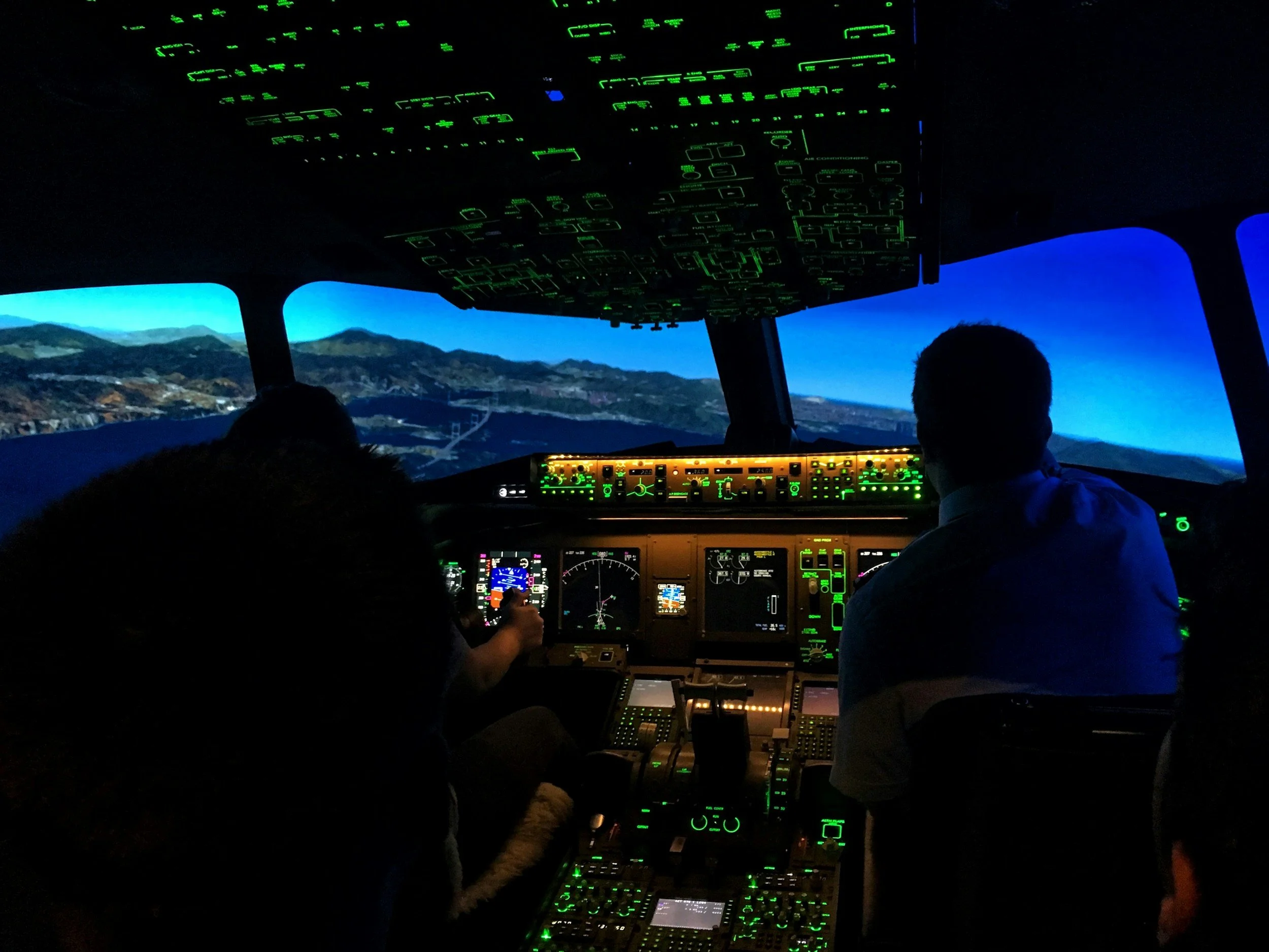 Inside the cockpit of an airplane during flight, with pilots and crew members monitoring instruments and controls, with mountain landscape visible through the windows.