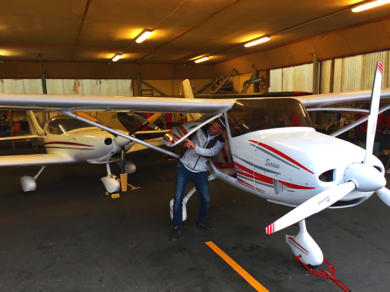 Person preparing a small white and red single-engine propeller airplane inside a hangar.