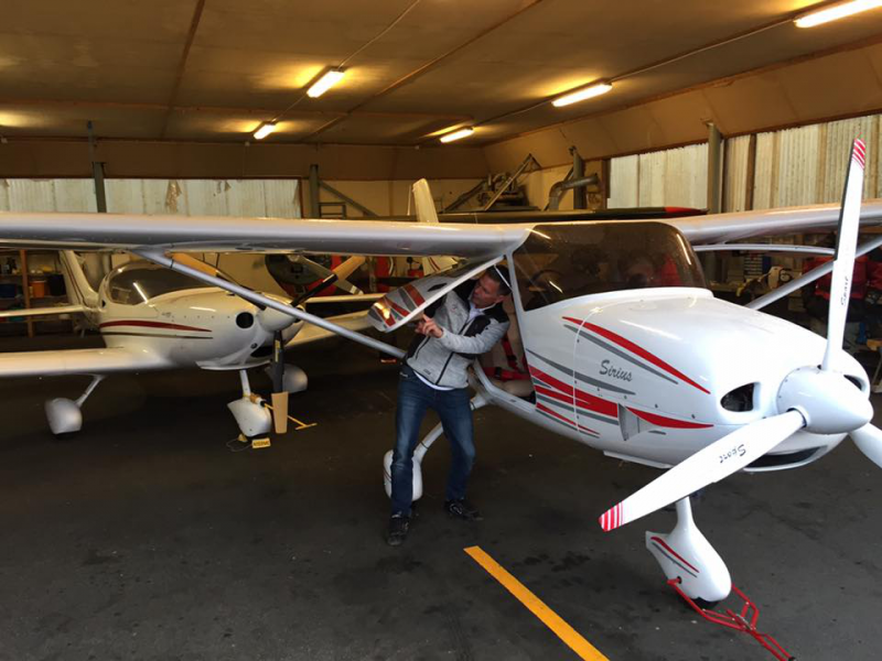Person standing next to and inspecting a small white and red propeller aircraft inside a hangar, with other similar aircraft in the background.