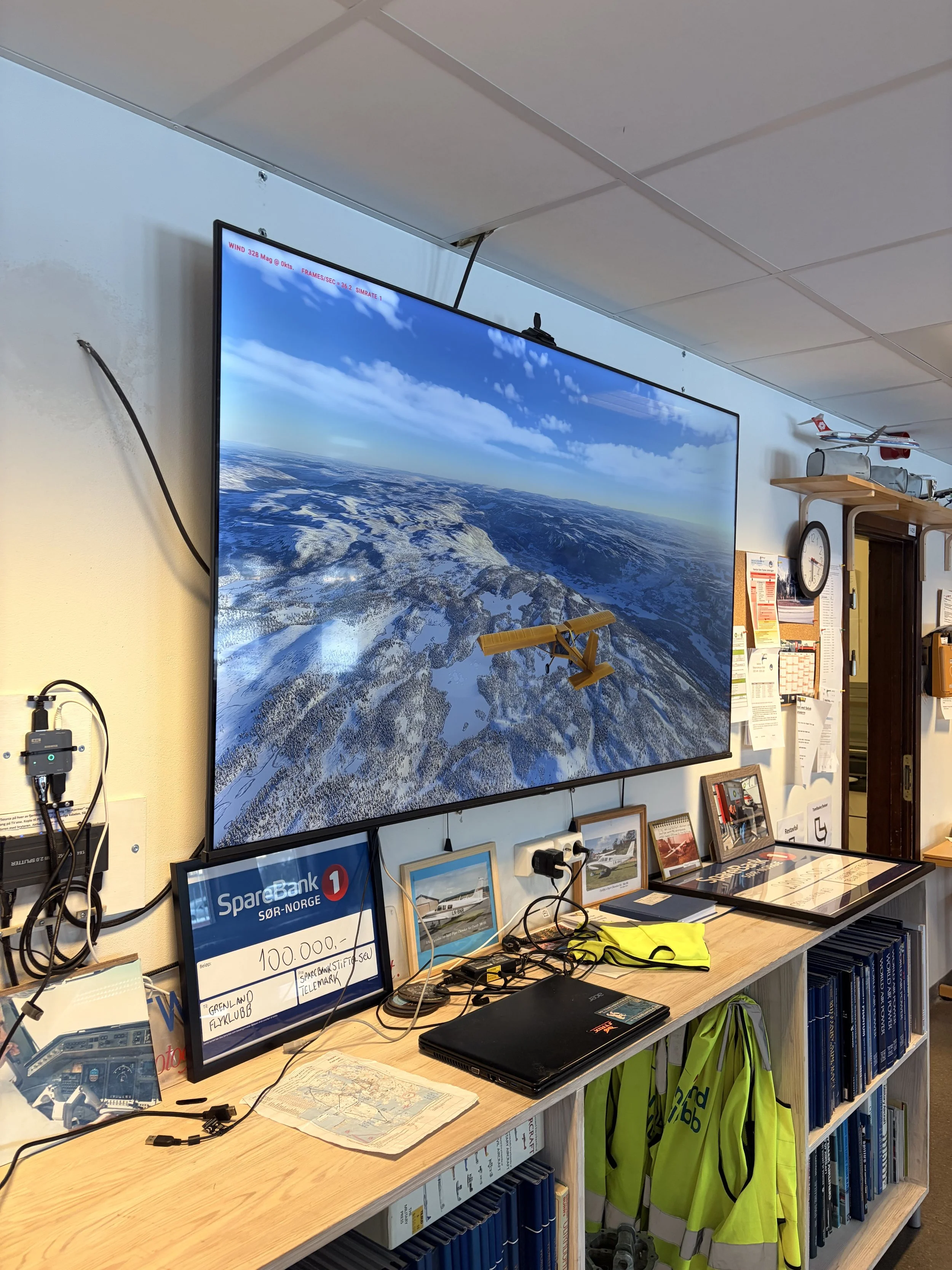 A large screen displays a flight simulation image of a winter landscape with snow-covered mountains and a small yellow aircraft flying above them.