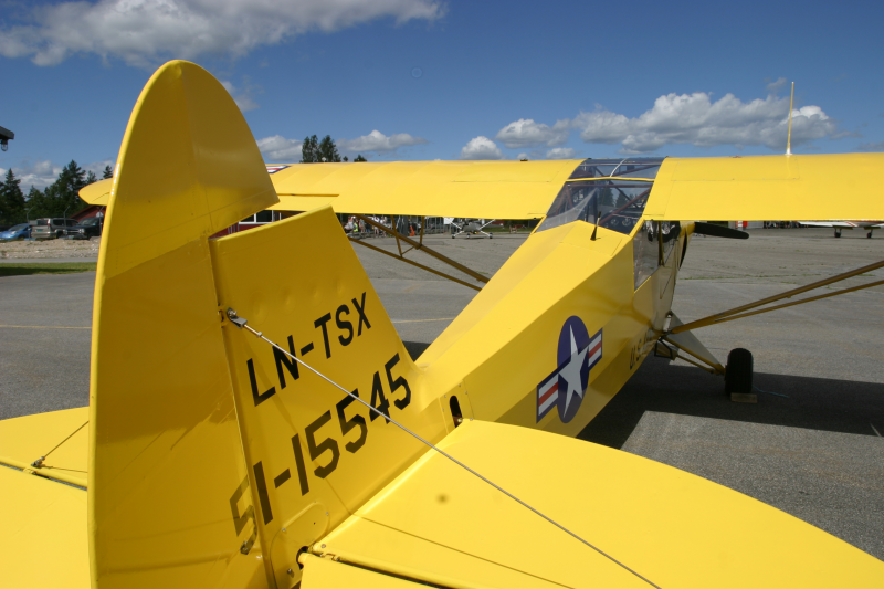 A yellow vintage military aircraft parked on an airfield with a blue sky and some clouds overhead.