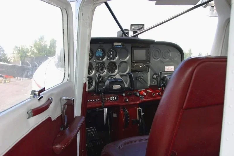 View of the cockpit of a small airplane with red leather seats and instrument panel.