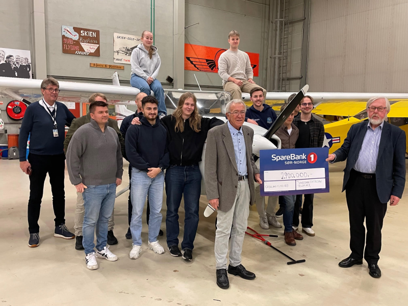 Group of people holding a large check in front of a small aircraft inside an airplane hangar.