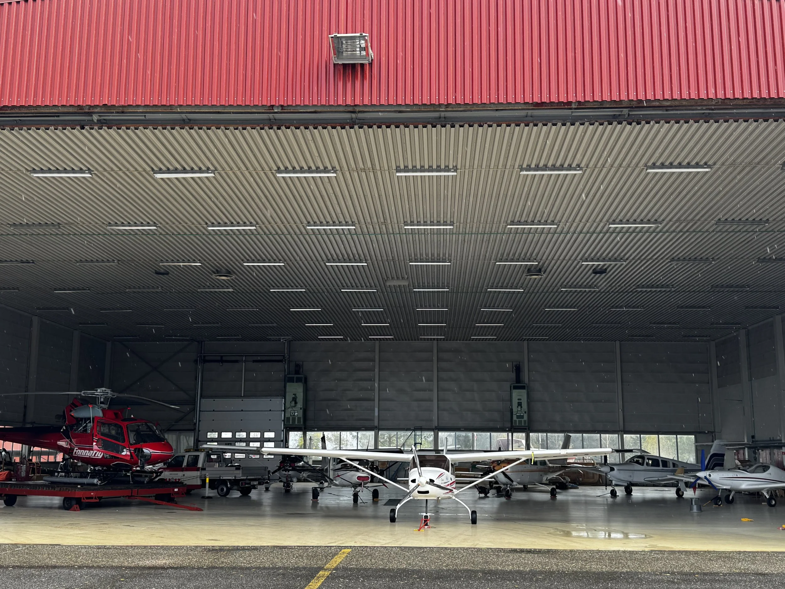 Inside of a hangar with several small aircraft and a red helicopter parked inside.