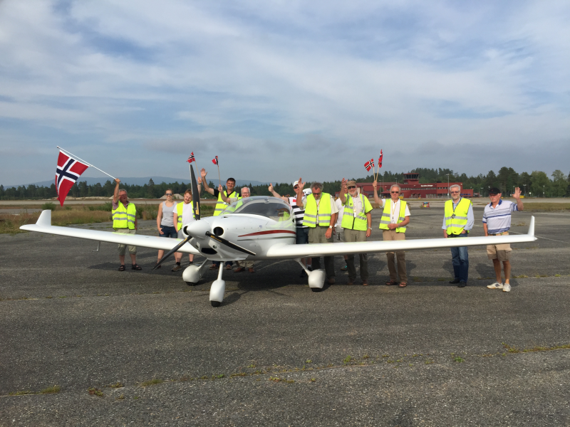 Group of people standing with a small private airplane on an airport tarmac, waving Norwegian flags.