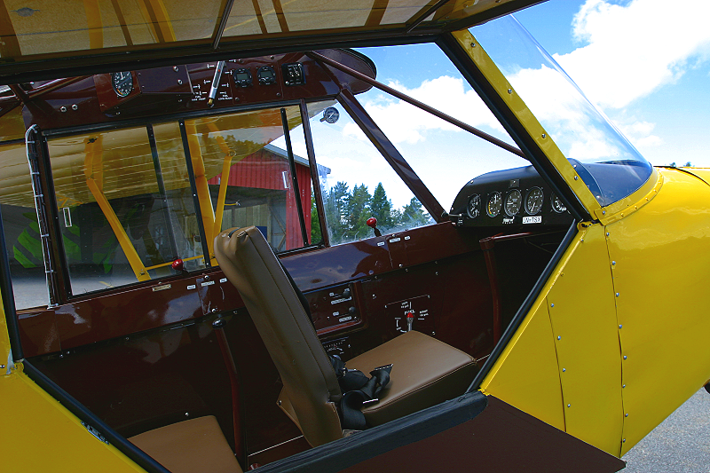 Interior of a vintage yellow airplane, showing the cockpit with brown leather seats, instrument panel, and controls.